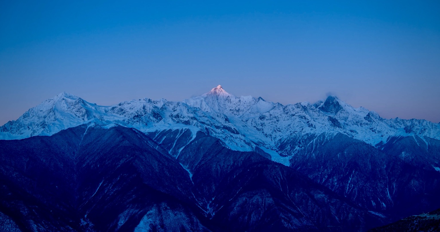 Snow-covered peaks of Meili Snow Mountain beneath a clear blue morning sky.